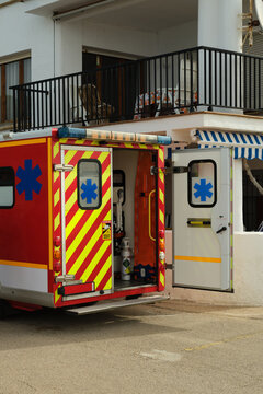 Ambulance vehicle with open rear doors showing medical equipment inside, parked near a residential building during an emergency call.