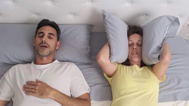 Middle aged couple in bed with man snoring and woman unable to sleep