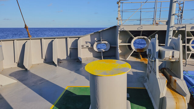 Close up view of yellow mooring bollard post and fairlead chocks on ship bow deck with blue ocean horizon background for maritime navigation transport concept