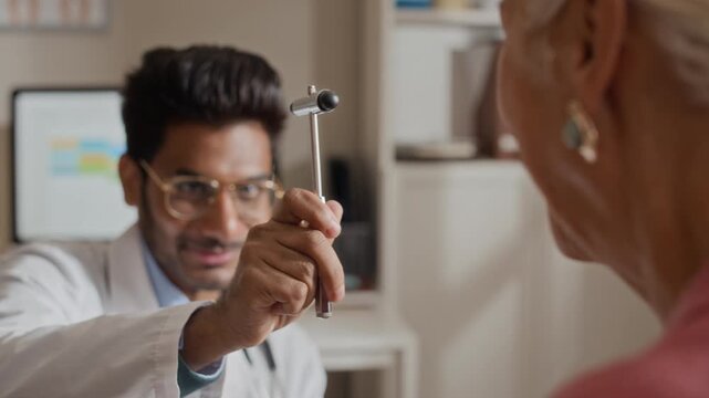 Young adult South Asian doctor performing neurological eye tracking test with reflex hammer on senior Caucasian female patient. Clip is perfect for geriatric care and medical clinic advertising
