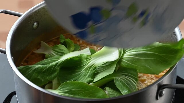 Putting bok choy into a pot of boiling spicy instant noodles soup 