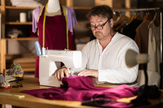 Man seamstress operating by sewing machine, manufactures clothing