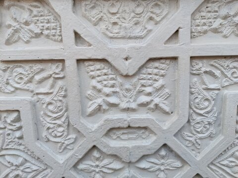 dAn ornamental relief featuring intricate geometric patterns integrated with detailed floral and botanical carvings, sculpted on a textured white plaster or stone surface, showcasing traditional archi