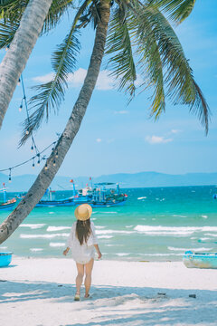 Woman Standing Beneath Palm Trees Facing the Sea