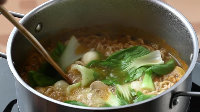 Stirring spicy instant noodle soup with bok choy, mushrooms, quail eggs and tteokbokki in a boiling pot