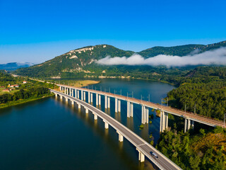 Fototapeta premium View of a bridge over a river with mountains and blue sky in the background in the early morning hours