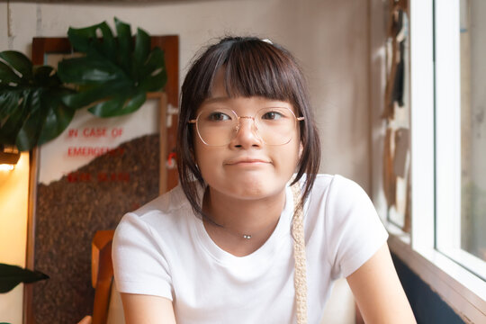 Young Asian woman with glasses pouting slightly, looking away in a casual indoor setting.