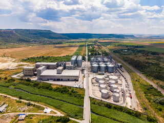 View of a large industrial facility with silos and tanks located near a green area under a cloudy sky in daytime © DSMT