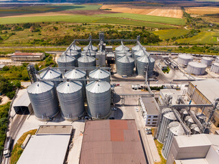 Multiple grain silos are seen from above in a farming area with green fields nearby during daylight hours © DSMT
