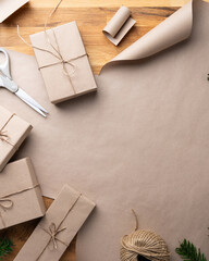 Obraz premium Top view of handmade Christmas gift wrapping with kraft paper, twine and evergreen branches on rustic wooden background with copy space.