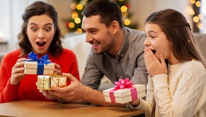 Obraz premium Happy family opening Christmas presents together at home, parents and daughter surprised by holiday gifts for winter celebration and festive tradition