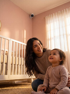 Mother and toddler in nursery with security camera. Parent watching baby in home bedroom.