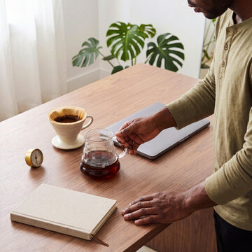 Man pouring pour-over coffee at desk. Male freelancer preparing morning brew in home office.