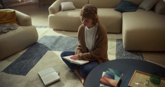 Calm Home Study Moment as a Young Woman Reads a Book on a Living Room Rug. Creative Overhead-to-wide Camera Movement Capturing Focused Leisure and Mindful Learning at Home.