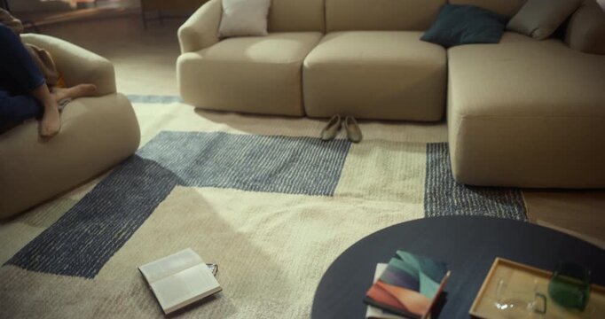 Dynamic Spiral Camera Drifts From an Open Book Lying on Living Room Rug to a Relaxed Woman Using Her Smartphone on the Sofa. Home Study, Reading, Social Media and Digital Leisure.