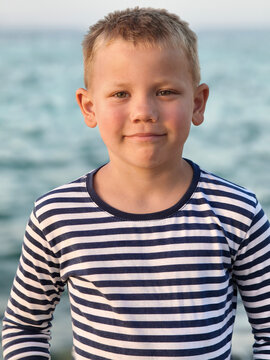 Young boy in a classic striped shirt stands confidently sea, his varied expressions capturing curiosity, contemplation, and carefree joy timeless portrait that tells story of childhood by shore.