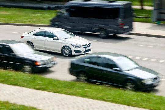 Minsk, Belarus - May 28 2021: White Mercedes-Benz CLA sedan C117 driving fast in city street traffic with motion blur background. German luxury vehicle moving on urban road among blurry automobiles.
