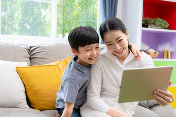 Fototapeta premium Cheerful mother and her young toddler using a touch screen tablet at home, representing digital parenting, early learning, and happy family time.