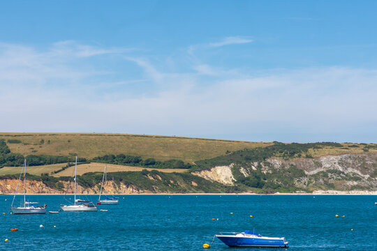 Swanage, UK - July 3rd 2026: Sailboats and motorboat moored in Swanage Bay with the Ballard Downs in the background.