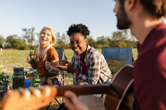 Friends Gather Around a Camp Enjoying Drinks, Music, and Laughter During a Sunset Camping Trip