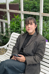 Fototapeta premium Vertical Portrait of Asian Person Sitting on Outdoor Bench Looking at Camera