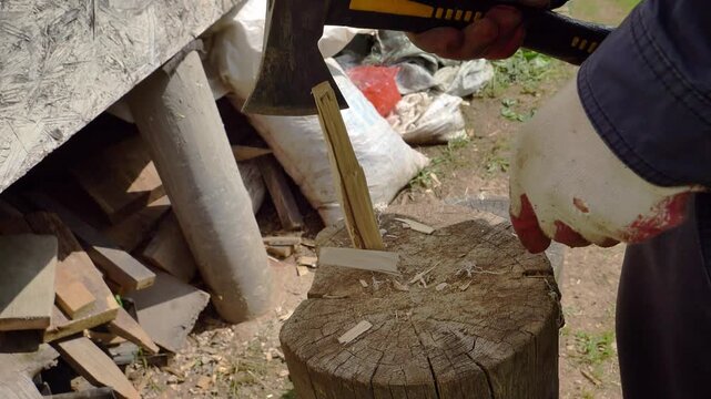 A close-up view captures a person splitting a small wooden stick with an axe on a chopping block, suitable for illustrating rural life or manual work.