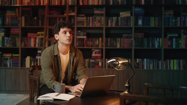Male journalist writing an article on laptop in a library, freelance work