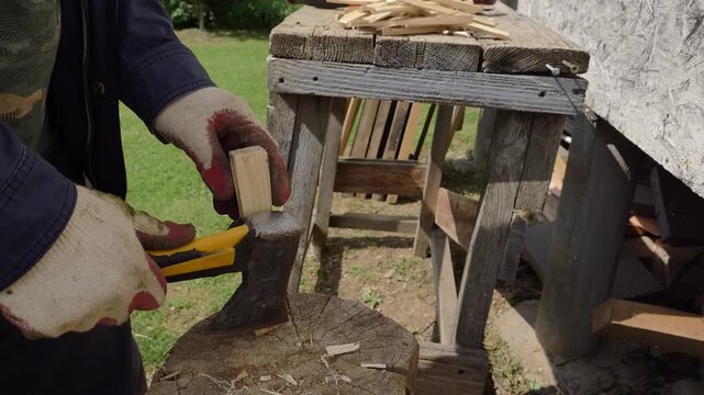 A close-up view of a person using a hatchet to split a small piece of wood on a tree stump outdoors during daylight for tasks like kindling or woodworking.