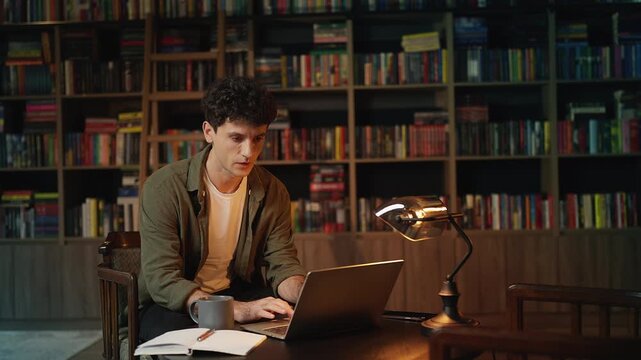 Focused male writer working on his book on laptop in a cozy coffee shop