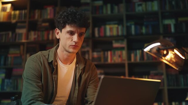 Young male historian typing on laptop in library, working on research project