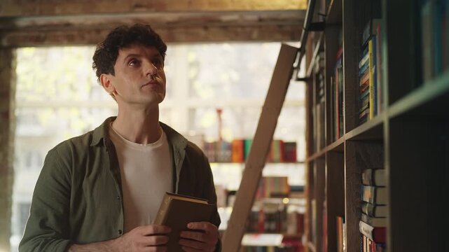 Focused young man choosing literature from shelves in a modern bookshop