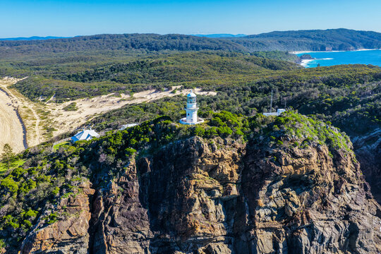 Aerial view of the historic Seal Rocks Lighthouse overlooking the rugged coastline, deep blue ocean and surrounding coastal landscape at Seal Rocks, NSW, Australia.