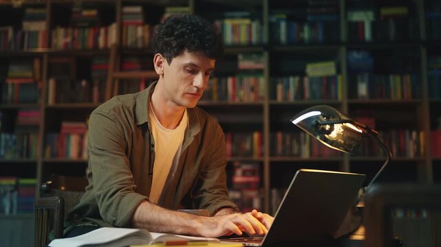 Young male interpreter studying literature and working on laptop in library