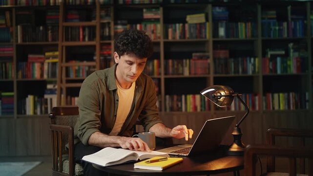 Young male student researching academic material on laptop in a library
