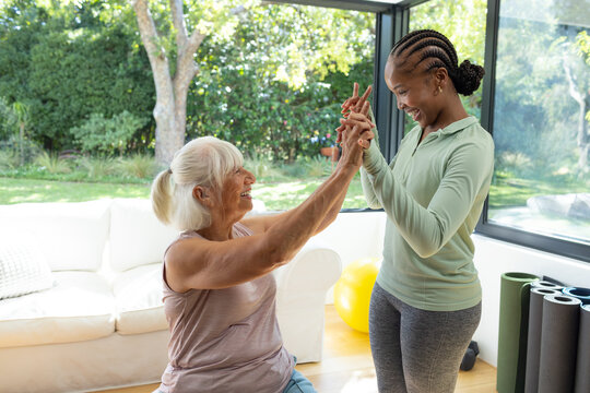 Senior woman and African American woman guiding hands at home wearing athletic top with yoga mats
