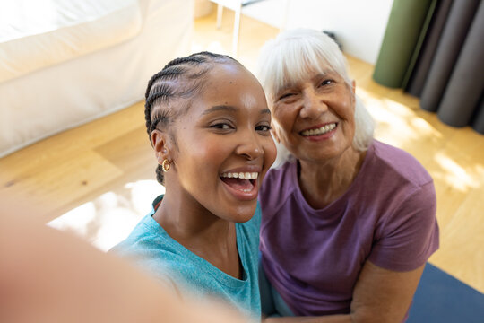 African American teal-shirted woman and senior woman leaning taking smartphone on blue mat at home