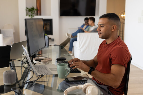 Male coworkers working at home, glass desk with laptop; others using phones on sofa, copy space