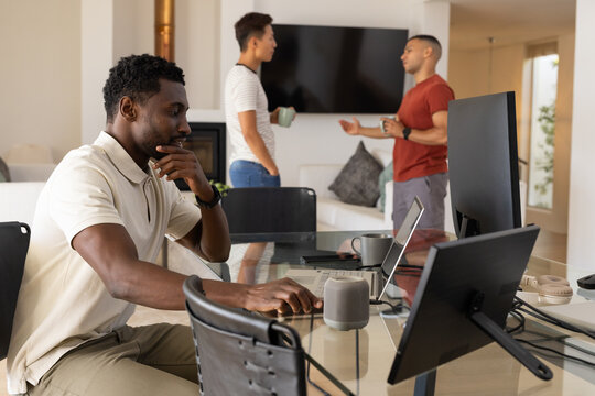 Diverse coworkers working at home; seated African-American man at laptop, two with mugs, copy space