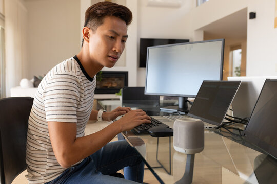 Middle-aged Asian man typing at glass desk with laptop, external monitor, striped shirt, copy space