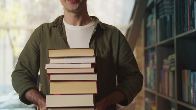 Portrait of male student holding stacks of books in university library