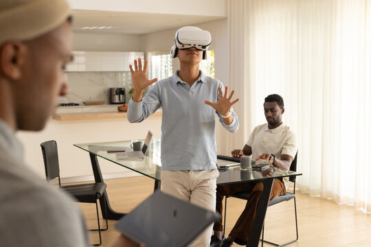 Diverse male coworkers testing virtual reality headset, using laptop and tablet at home dining area