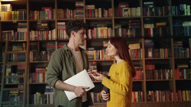 Young red-haired woman and male librarian discussing a book in library