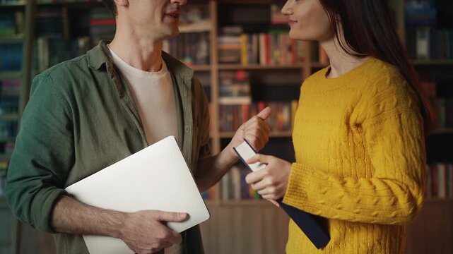 Smiling male and female students discussing research in university library