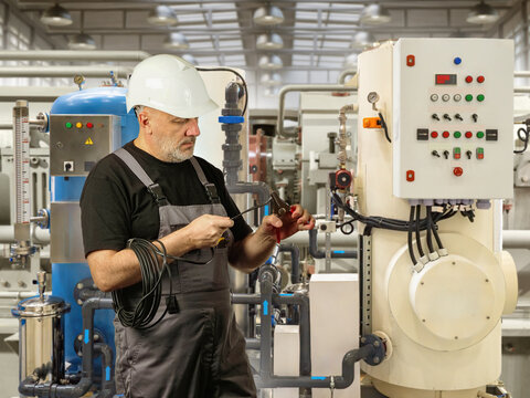 Industrial engineering. Maintenance technician inspects and tests automated control equipment during servicing operations at a manufacturing plant.