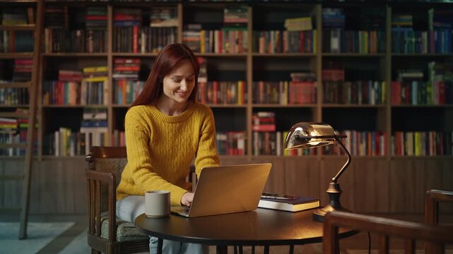 Inspired red-haired female author writing her book on laptop in coffee shop