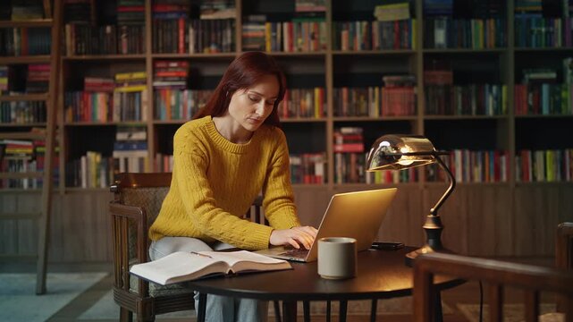 Young red-haired female scientist doing research on laptop in coffee shop