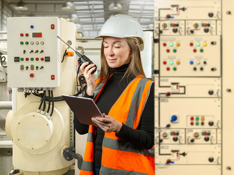 Industrial automation. Female engineer inspects electrical control equipment at industrial facility using tablet and radio communication system.