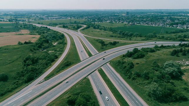 Aerial view of a complex highway interchange surrounded by green fields and scattered suburban development.