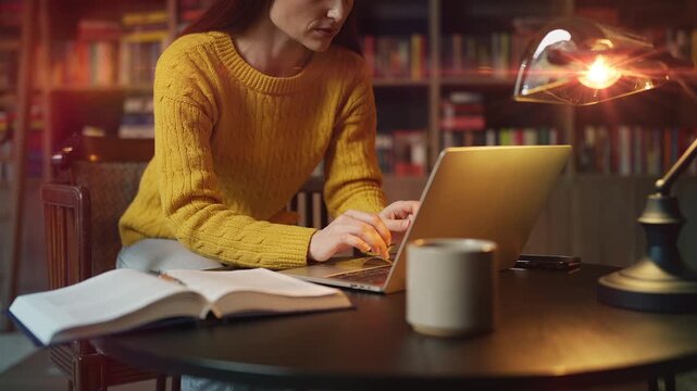Concentrated red-haired woman working on laptop and researching in library