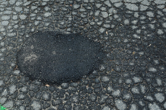 Close up view of damaged asphalt pavement with alligator cracking and a freshly patched pothole marked with green spray paint. Urban road maintenance, infrastructure repair, and street restoration con